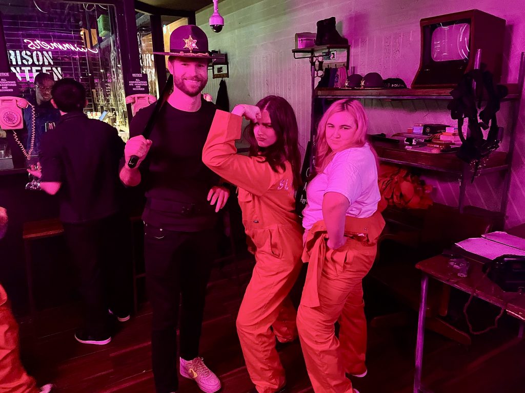 Paul, Abi, and Georgiana are embracing the prison themed bar in orange jumpsuits 