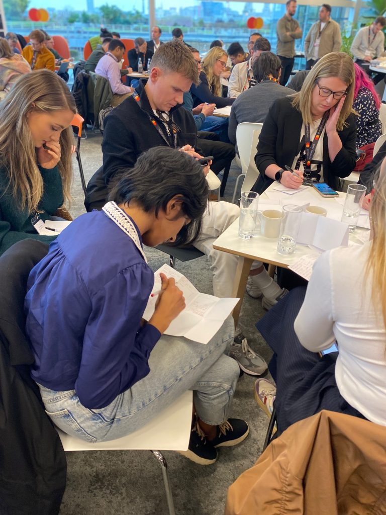 Participants at Primark's ideation workshop working on the Crazy 8's exercise. They are folding sheets of paper into eight sections and sketching eight distinct ideas, focusing on rapid ideation and creativity. 