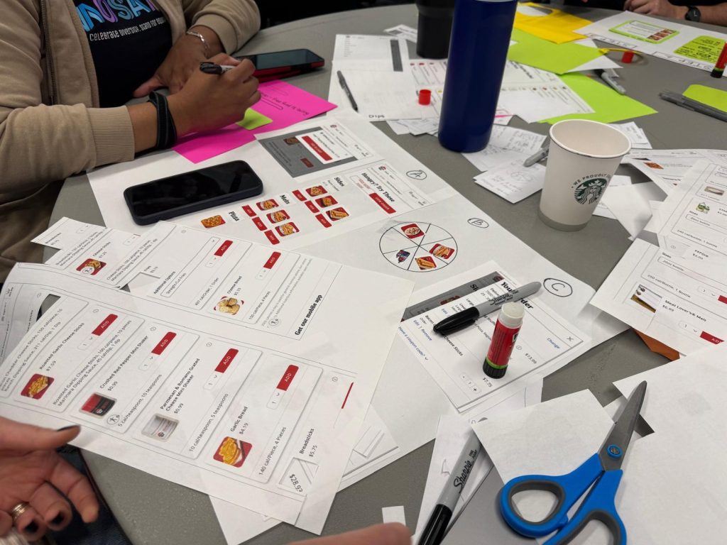 A glimpse of one team working on their paper prototype with paper, scissors and glue on the table as they construct the prototypes.